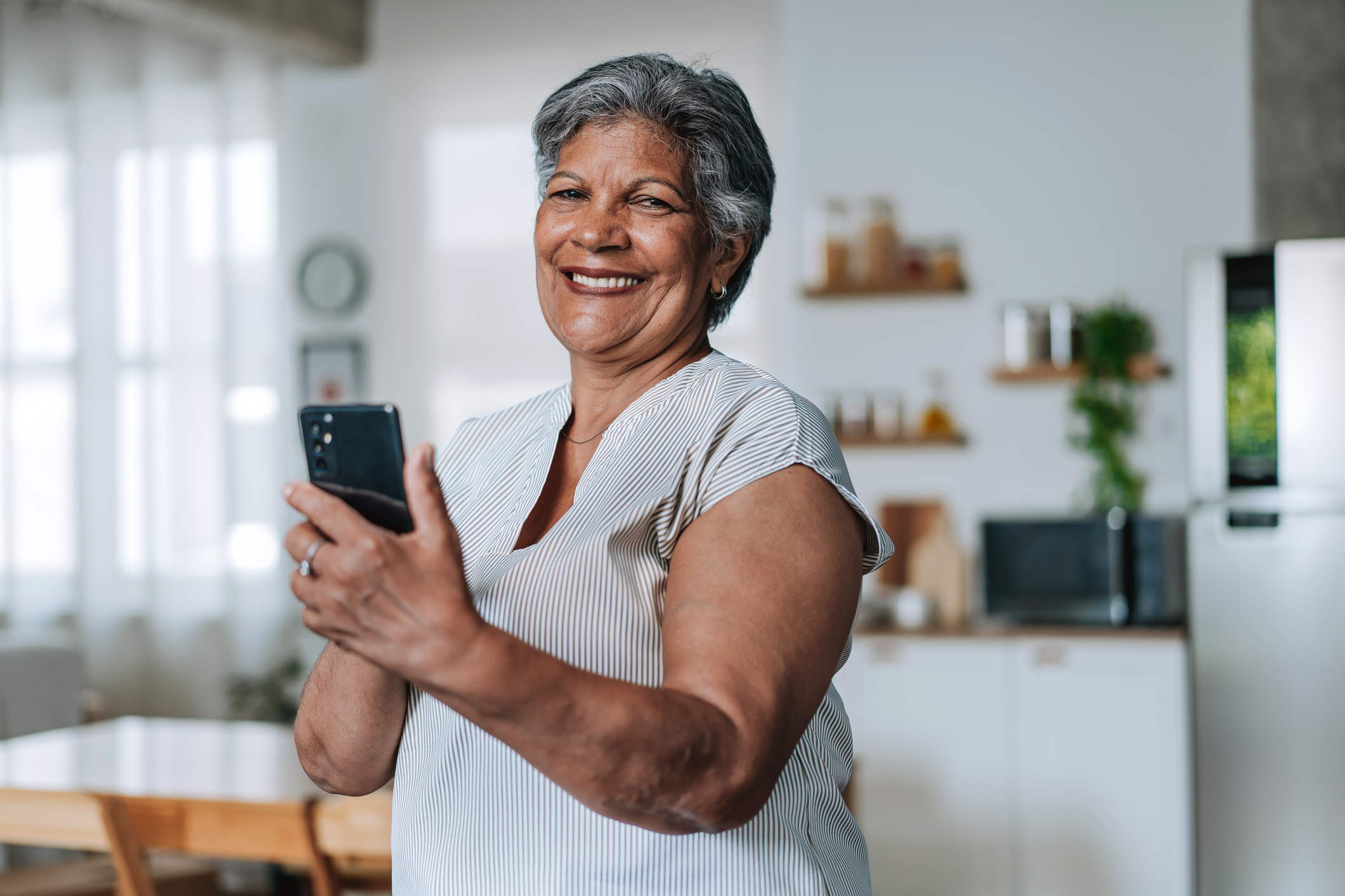 Mulher madura sorrindo com um celular nas mãos, em casa.